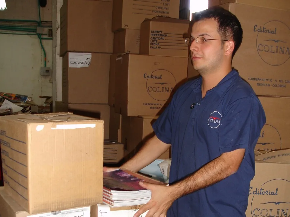 Persona organizando cajas de impresos en una bodega durante una entrega de producción litográfica